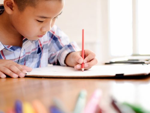 A kindergartener sitting at a desk coloring in a book