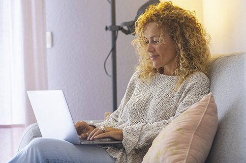 Relaxed and happy adult attractive woman working at home with laptop computer comfortably sitting on the sofa - concept of modern people and home work activity - independent lady use notebook online to surf the web