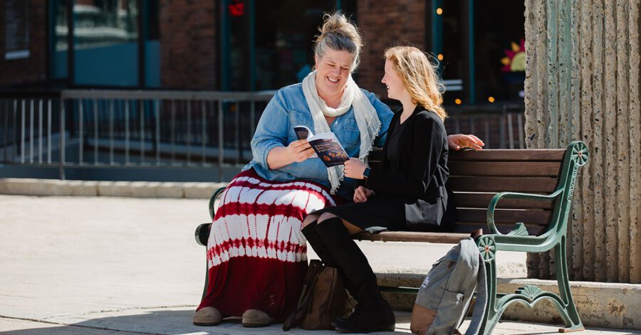Homeschool mother and daughter reading together on a bench.