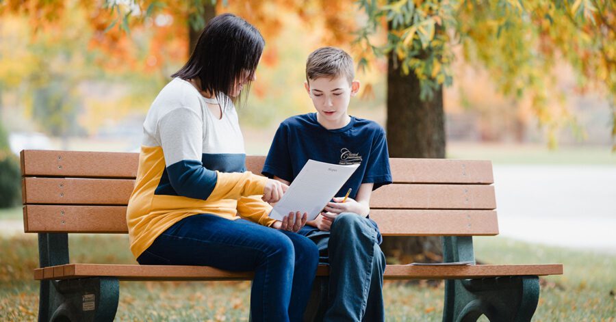 Homeschool parent and student studying on a park bench.
