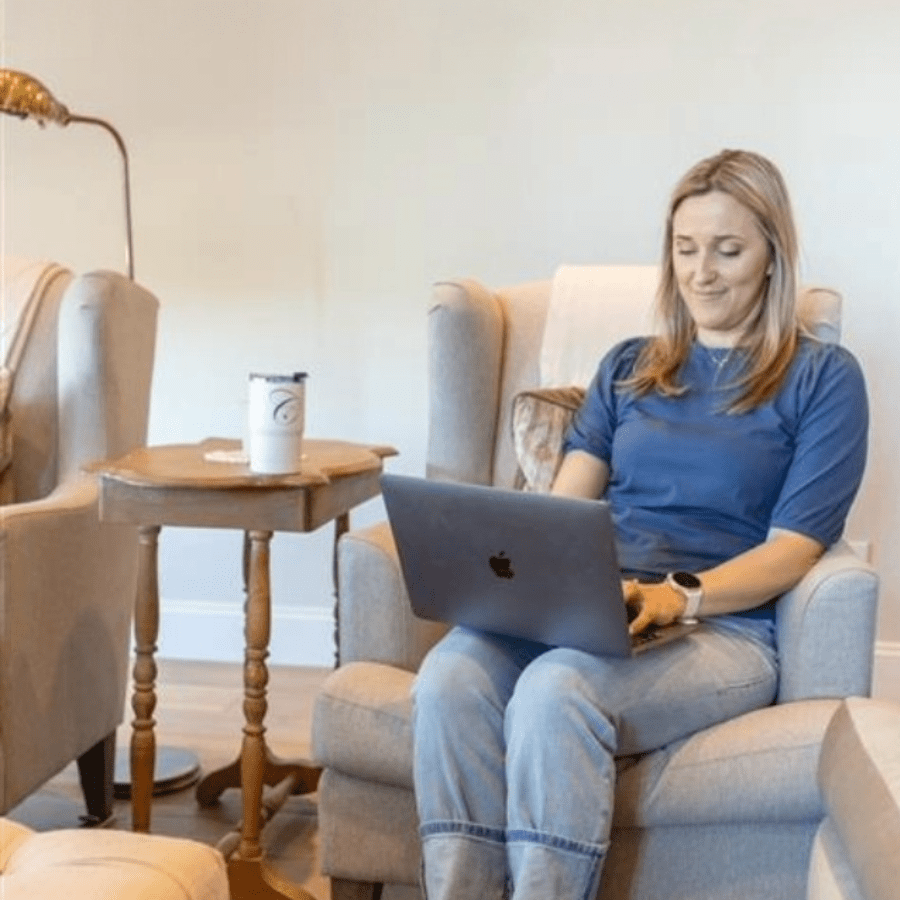 a young mom sitting on a chair working on a laptop