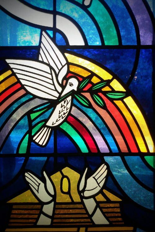 Stained Glass including a dove with olive branch and hands with a seed